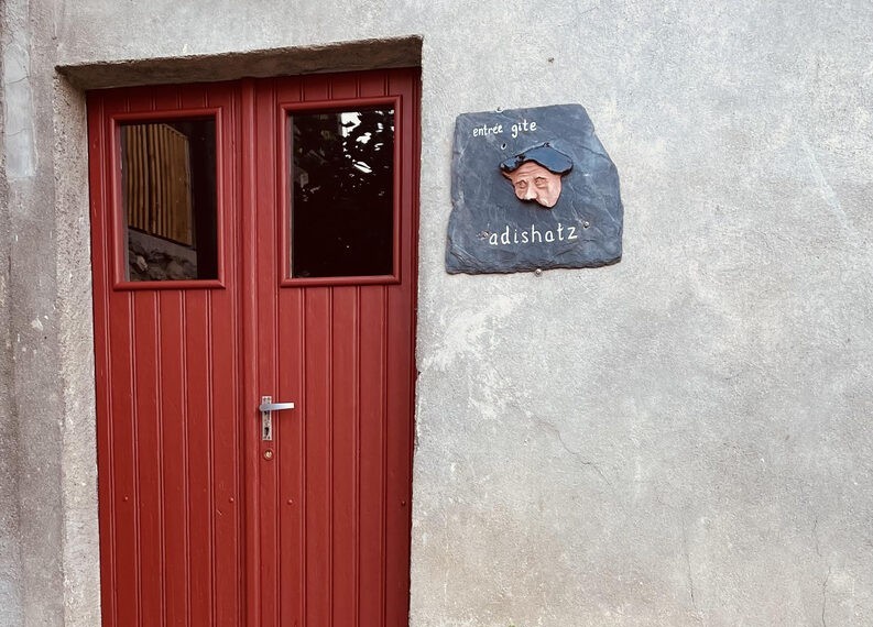 Entrée du gîte Adishatz, porte rouge et écriteau en ardoise